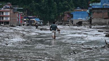 A resident walks along a street covered in mud following flash floods and a landslide disaster in Devghat, in Nepal's Nuwakot district on August 26, 2026. A massive flood and landslide disaster on the Nepal-Tibet border killed at least 103 people on August 26, 2026 and left several hundred missing, many of them foreign tourists. Aid workers said entire settlements had been "wiped out". Some 403 tourists -- 341 of them foreigners -- were unaccounted for several hours after the disaster struck, according to the tourism ministry.