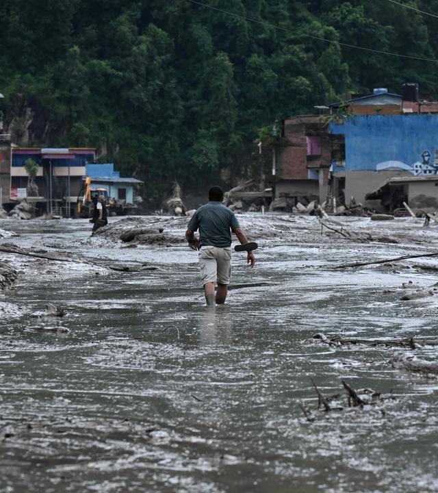 A resident walks along a street covered in mud following flash floods and a landslide disaster in Devghat, in Nepal's Nuwakot district on August 26, 2026. A massive flood and landslide disaster on the Nepal-Tibet border killed at least 103 people on August 26, 2026 and left several hundred missing, many of them foreign tourists. Aid workers said entire settlements had been "wiped out". Some 403 tourists -- 341 of them foreigners -- were unaccounted for several hours after the disaster struck, according to the tourism ministry.