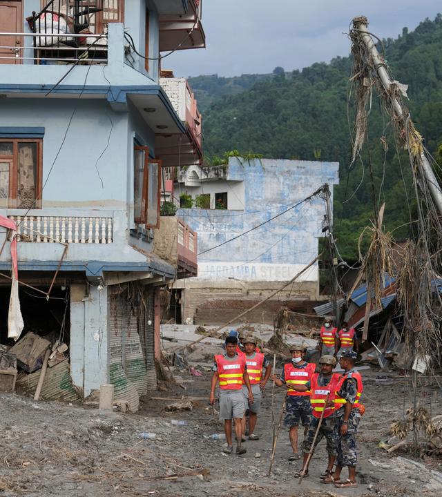 Rettungskräfte stehen nach einer Sturzflut im Gebiet Devighat neben beschädigten Gebäuden.