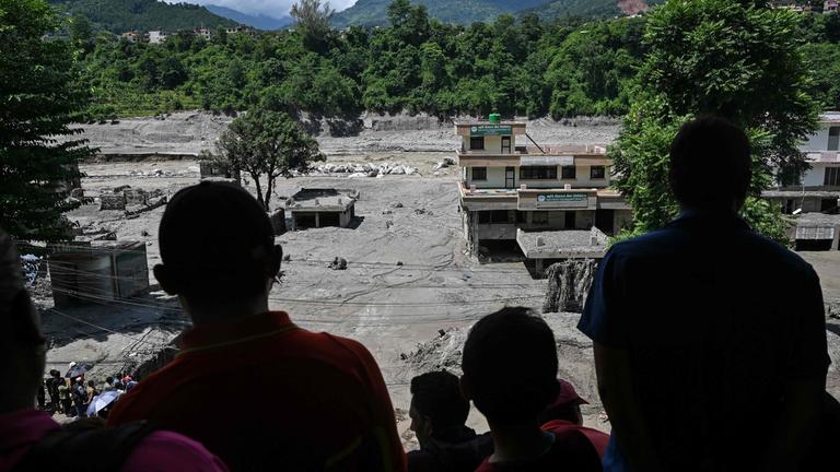 Menschen beobachten von einem Hausdach aus die von Schlamm überfluteten Häuser nach Sturzfluten in Trishuli im nepalesischen Distrikt Nuwakot am 27. August 2026. 
