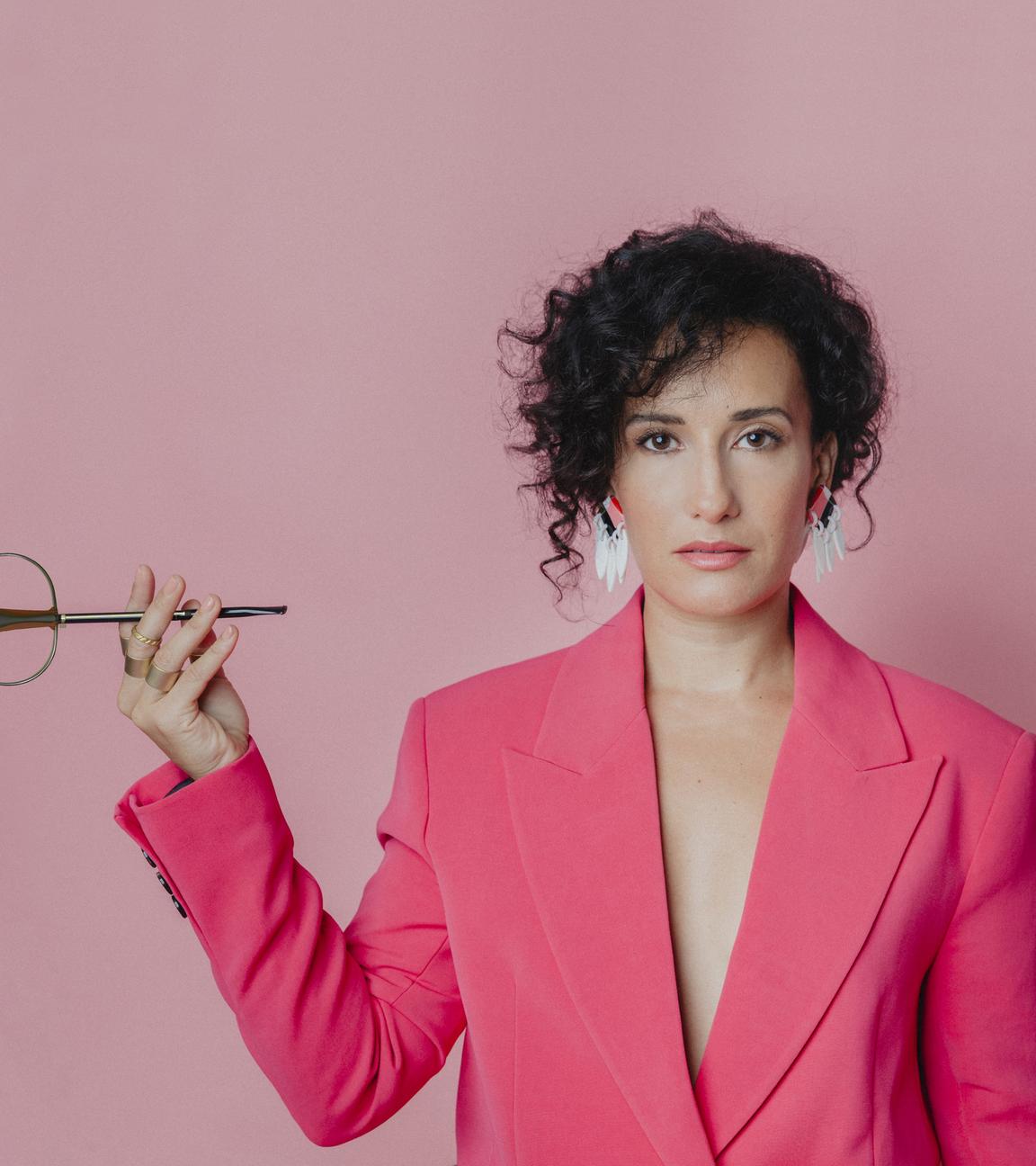 Die Musikerin Nesrine mit E-Cello vor pinkem Hintergrund