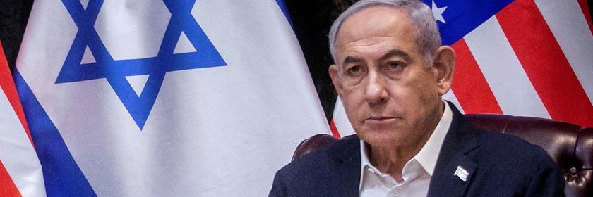 Benjamin Netanjahu, ein älterer Mann mit grauen Haaren, sitzt vor einer israelischen und einer US-amerikanischen Flagge in einer Pressekonferenz.