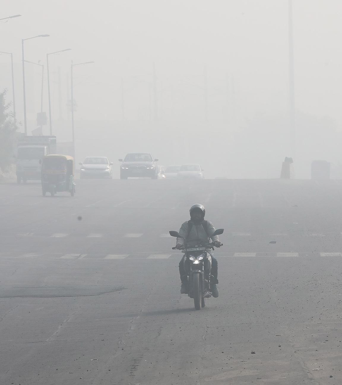 Ein Mann fährt am 15. Dezember 2025 auf einer breiten Straße inmitten dichten Smogs in der Nähe von Neu-Delhi, Indien, Motorrad. Die Sichtweite ist sehr gering.
