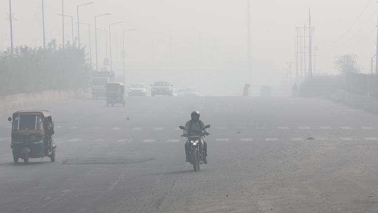 Ein Mann fährt am 15. Dezember 2025 auf einer breiten Straße inmitten dichten Smogs in der Nähe von Neu-Delhi, Indien, Motorrad. Die Sichtweite ist sehr gering.