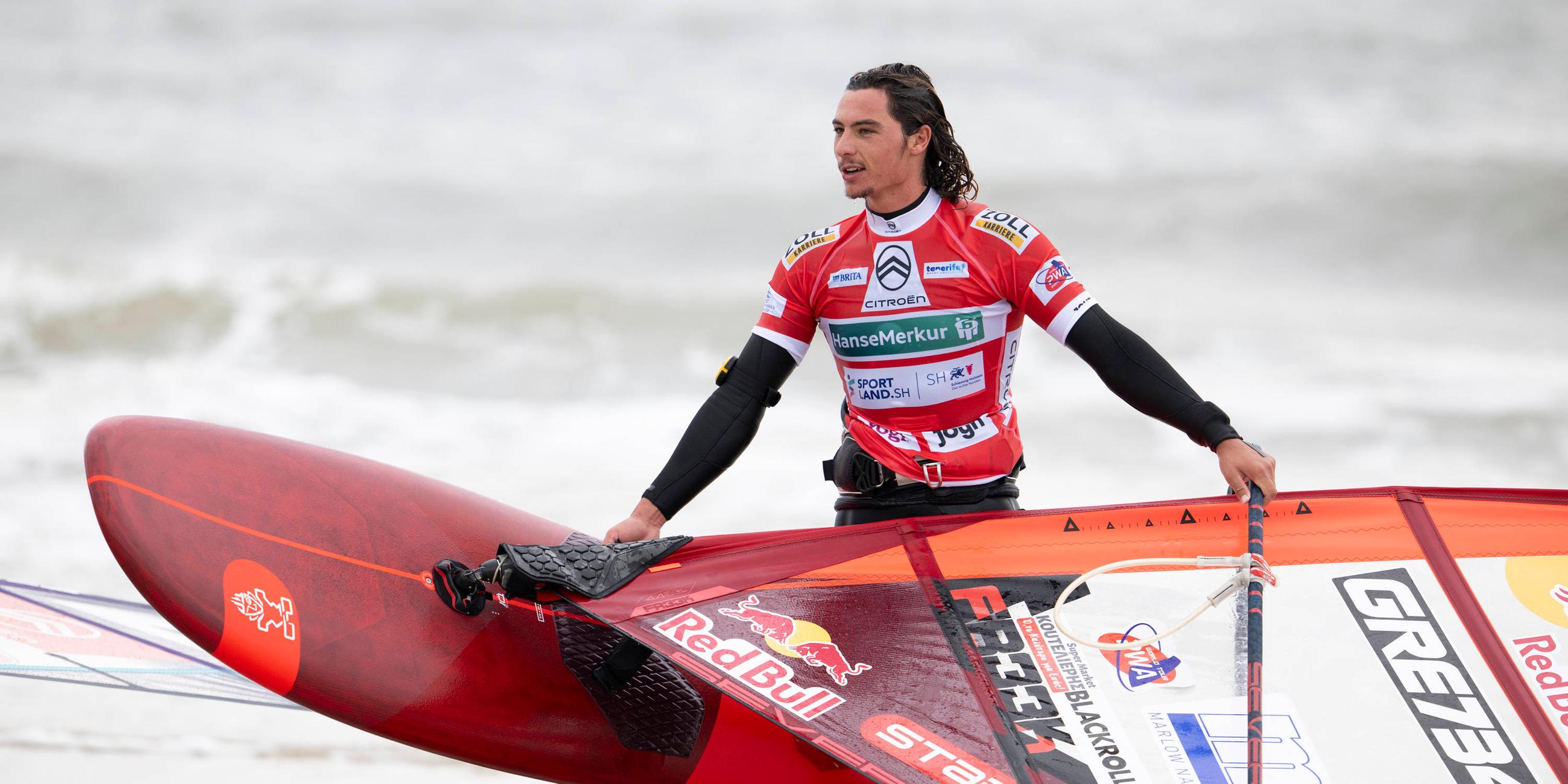 Lennart Neubauer trägt sein Windsurfbrett aus dem Wasser