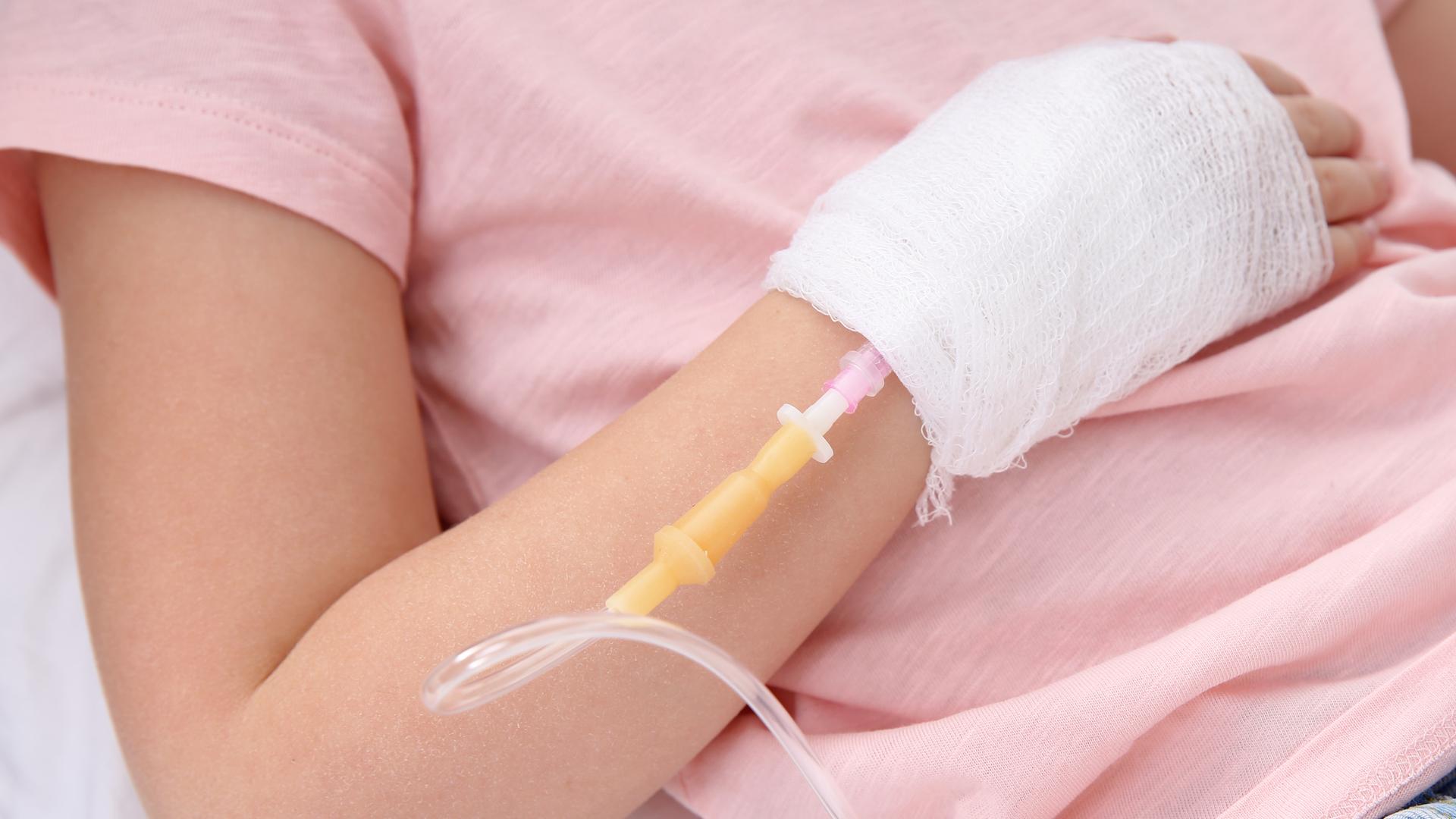 Ein Kind hat einen Infusionsschlauch und Verband an der Hand.