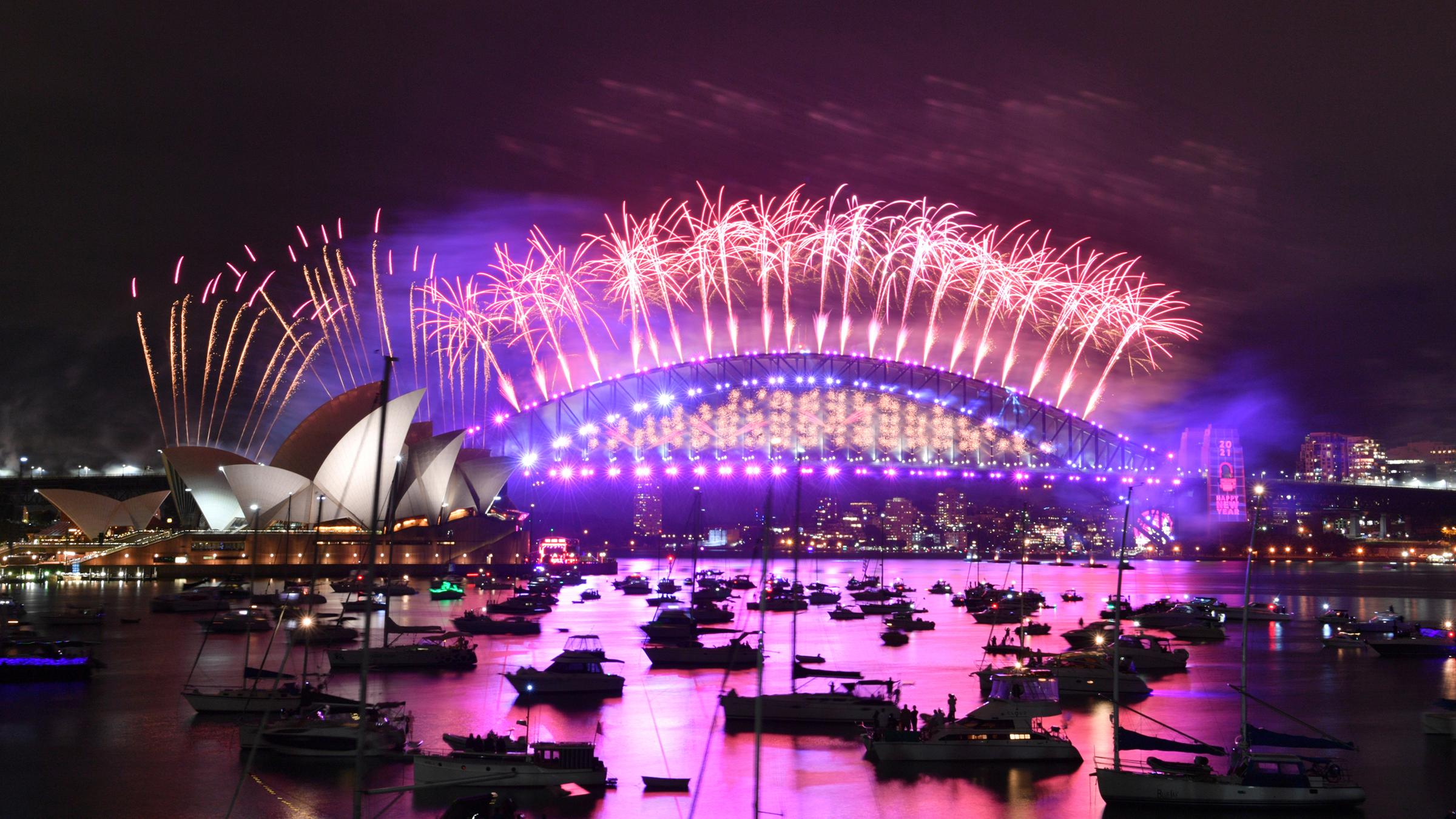 Im Hafen von Sydney treibende Boote werden vom Feuerwerk beleuchtet, das von der Harbour Bridge und dem Opernhaus (l) aus gestartet wird.