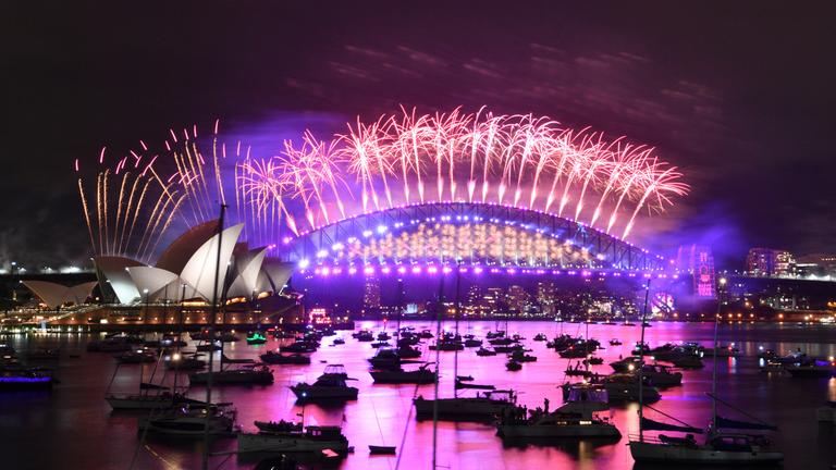 Im Hafen von Sydney treibende Boote werden vom Feuerwerk beleuchtet, das von der Harbour Bridge und dem Opernhaus (l) aus gestartet wird.