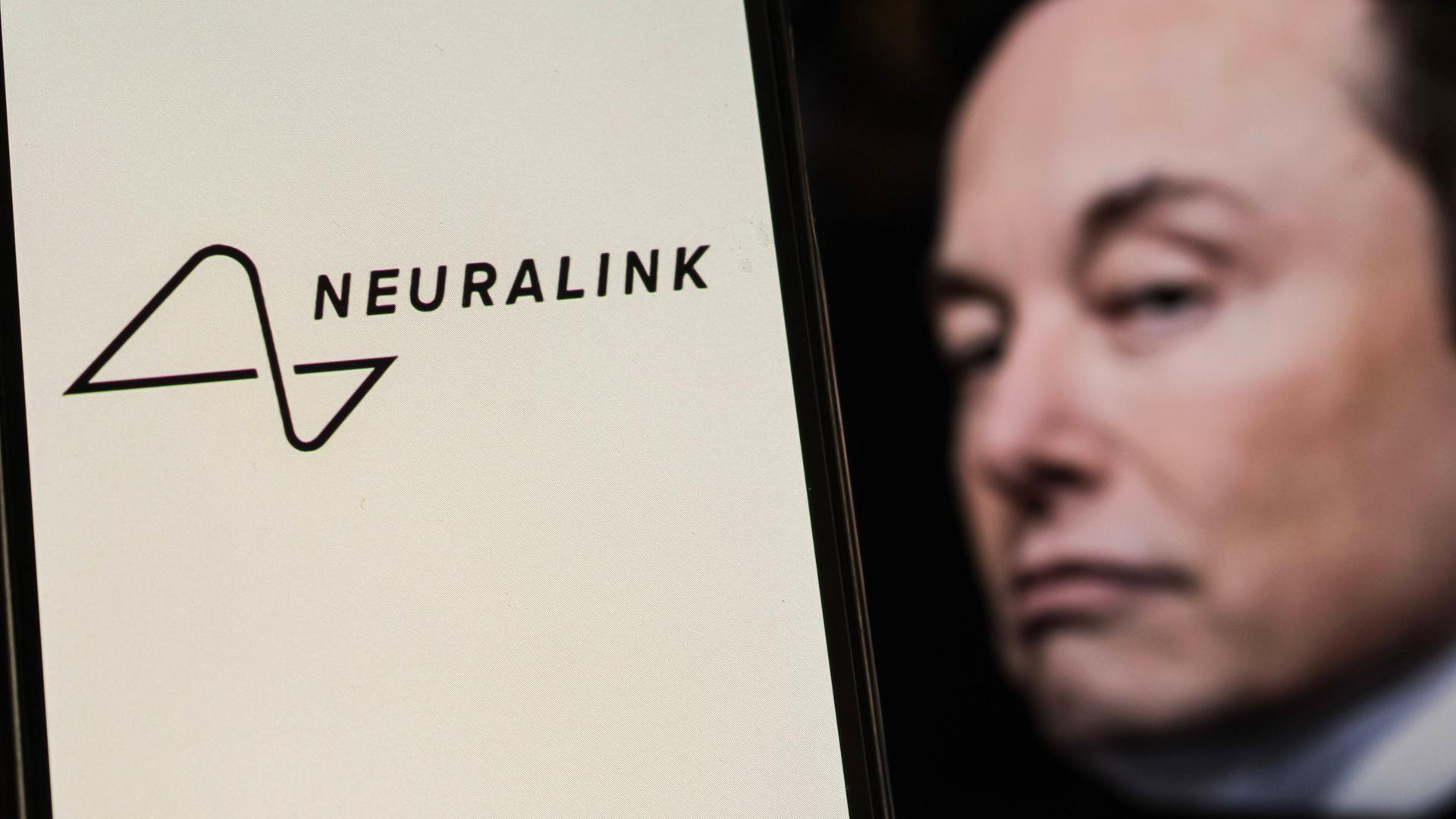 Das Neuralink-Logo ist auf einem Smartphone-Bildschirm mit Elon Musk im Hintergrund zu sehen. 