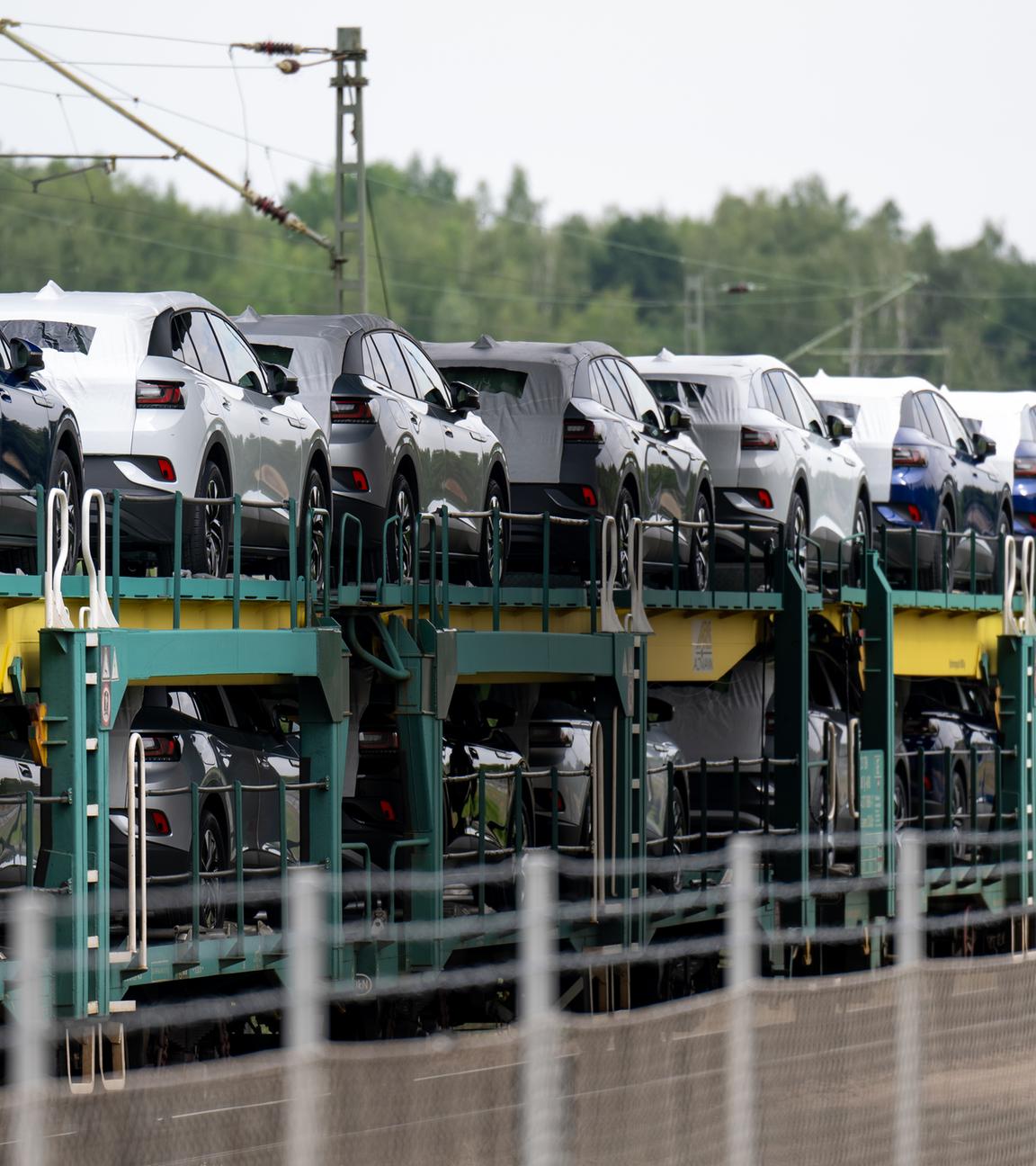 Ein Güterzug mit neuen Elektrofahrzeugen steht neben dem Werksgelände.