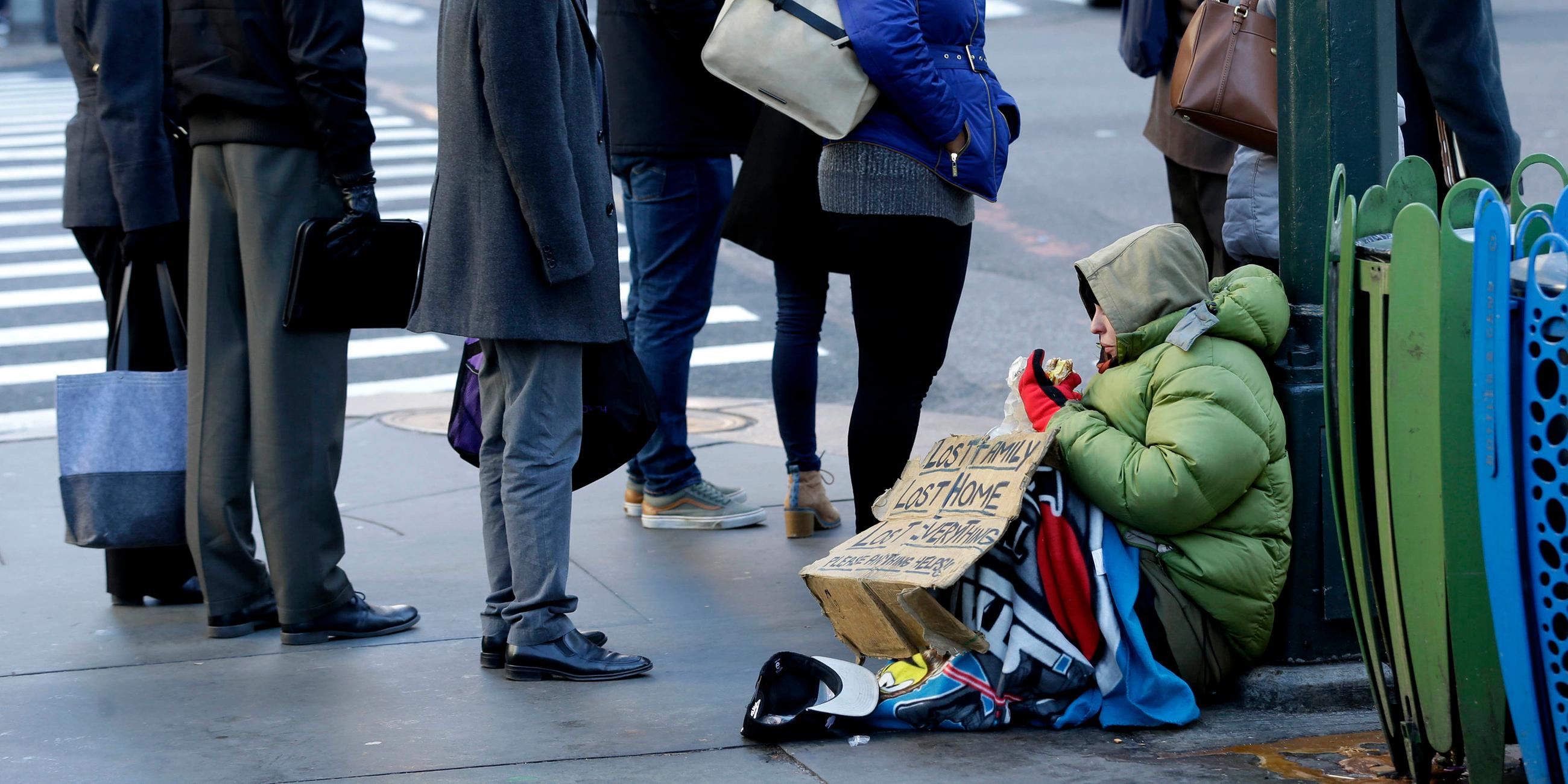 Eine obdachlose Frau sitzt im Winter in Manhatten, New York, an einem Straßenüerbgang und bittet Menschen mit einem Pappschild um eine Spende.