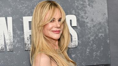 Schauspielerin Nicole Kidman lächelt auf einem roten Teppich vor grauem Hintergrund.