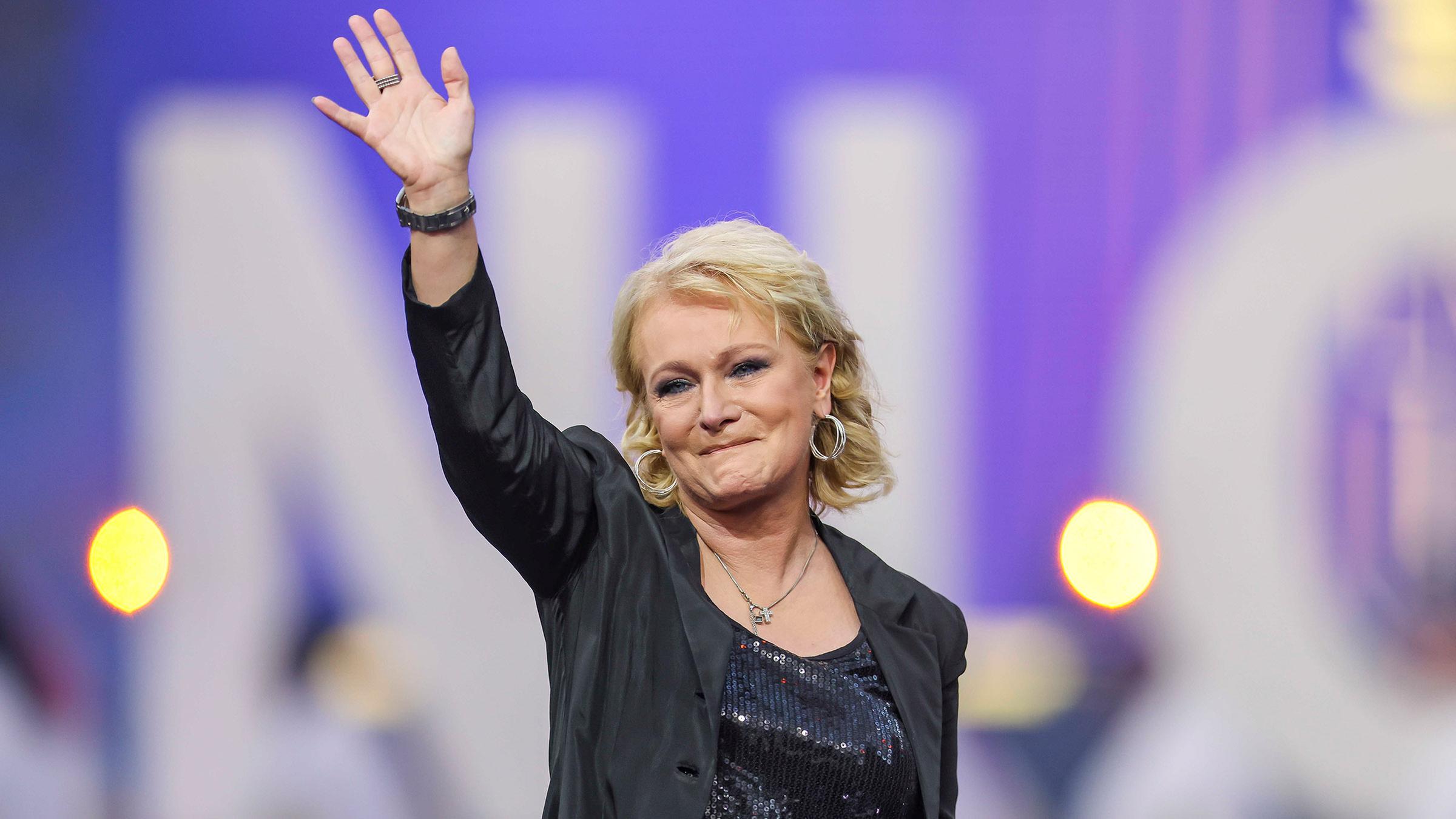 Sängerin Nicole winkt und schaut in die Kamera.