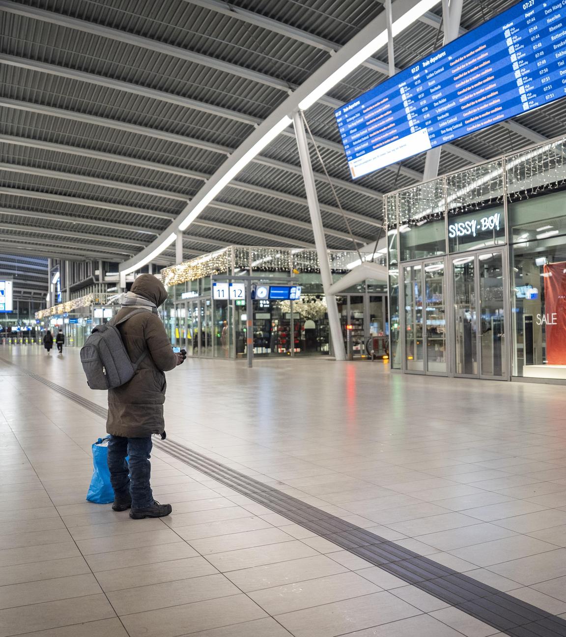 Eine Person schaut auf die Informationstafel am ansonsten fast menschenleeren Hauptbahnhof Utrecht.