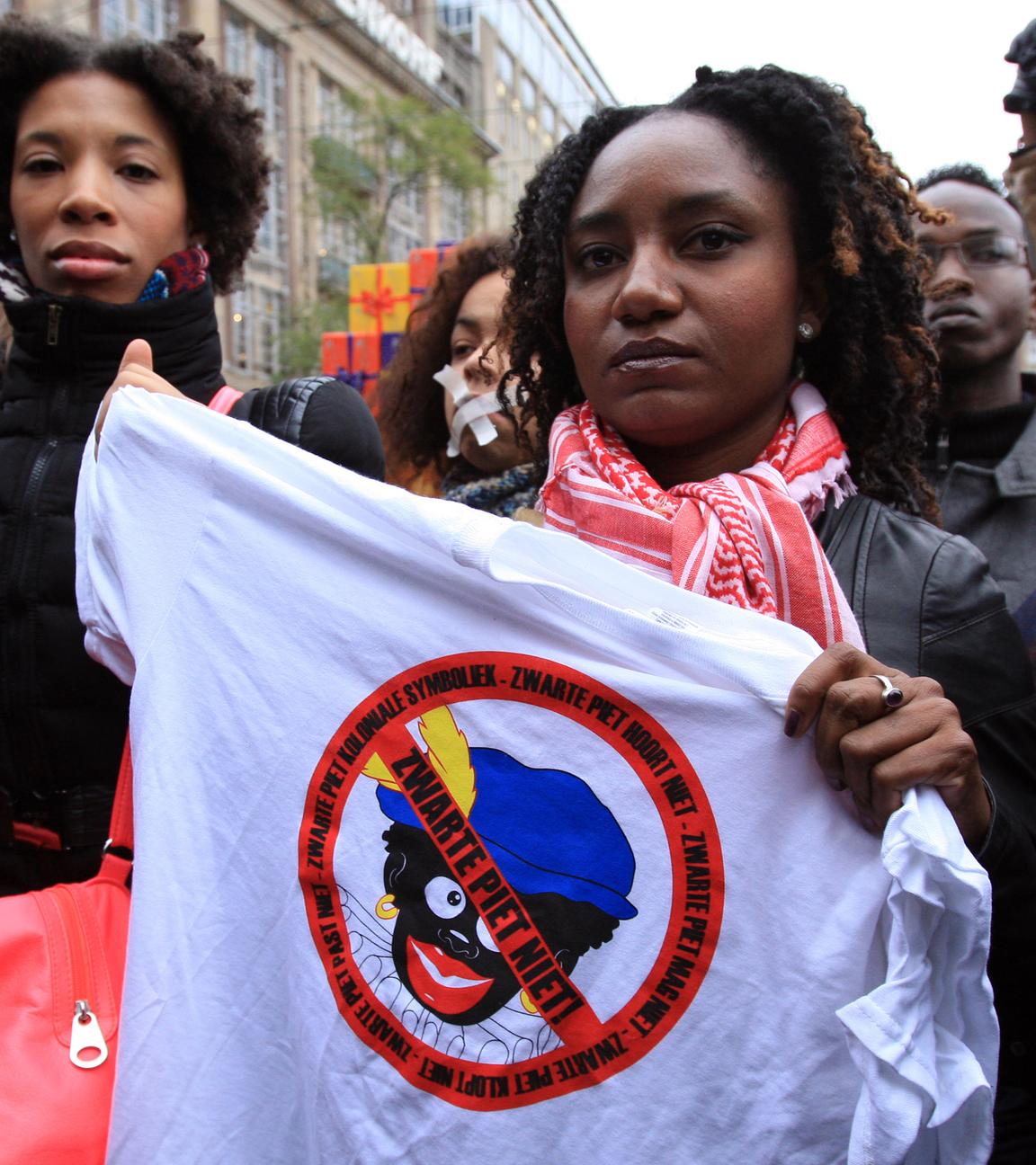 demonstration gegen den "schwarzer peter" in amsterdam. Aktivistin hält Banner in die Höhe gegen die Rassitische Nikolaustradition