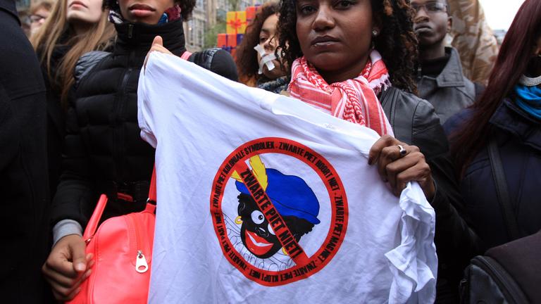 demonstration gegen den "schwarzer peter" in amsterdam. Aktivistin hält Banner in die Höhe gegen die Rassitische Nikolaustradition