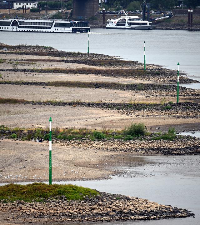 Ein Schiff fährt bei niedrigem Wasserstand auf dem Rhein an trocken gefallenen Buhnen vorbei.