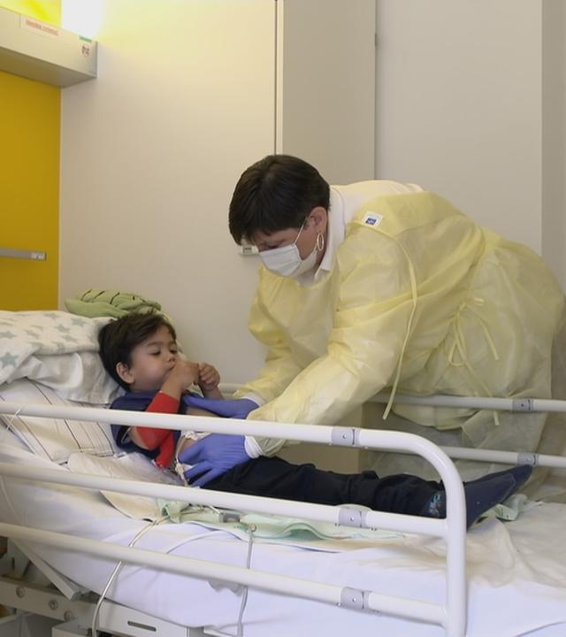 Pflegekraft brtastet Bauch eines Kindes auf Krankenbett