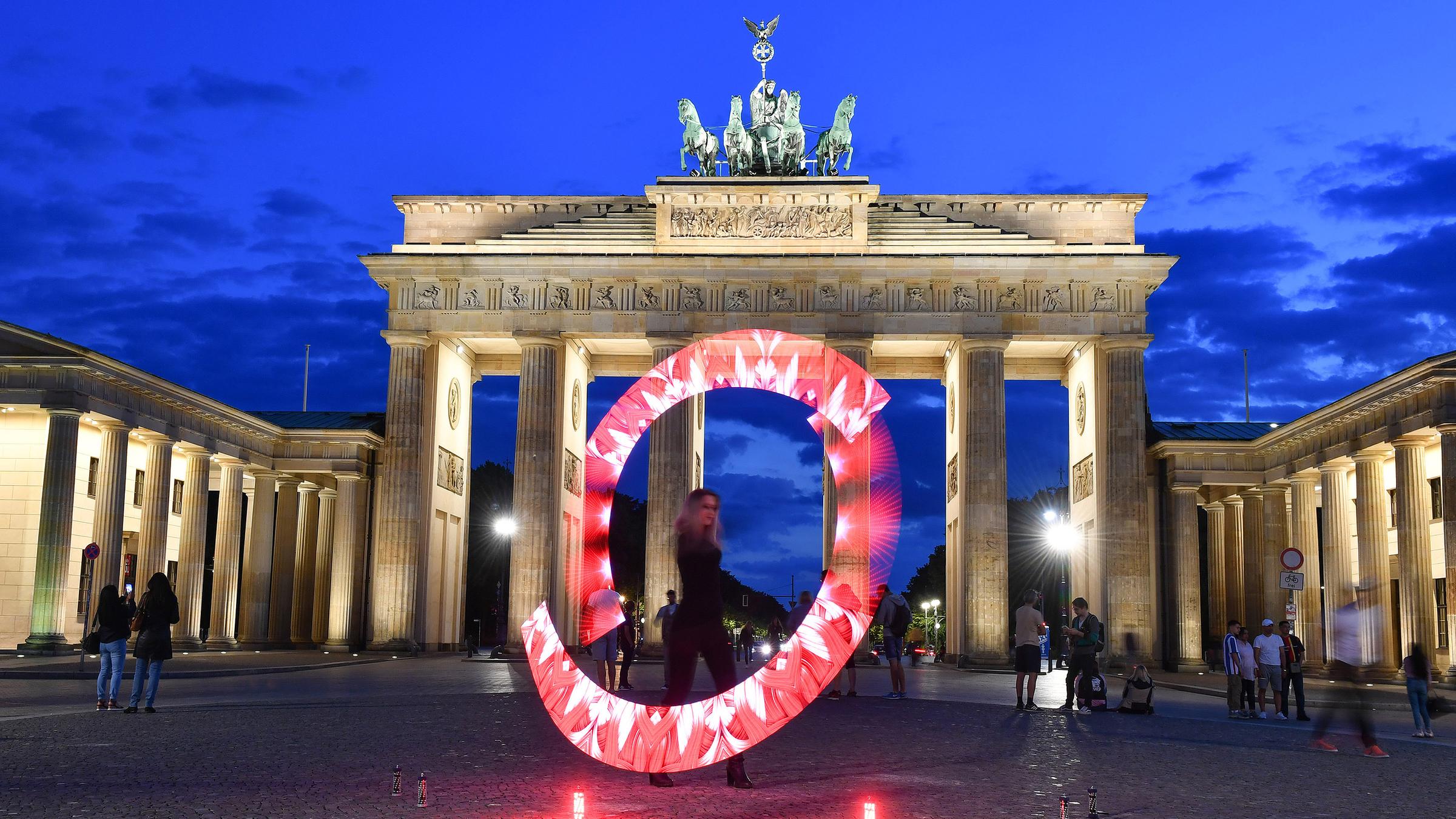 Eine Lichtkünstlerin zaubert mit roten Lichtern einen Leuchtkranz vor das Brandenburger Tor.