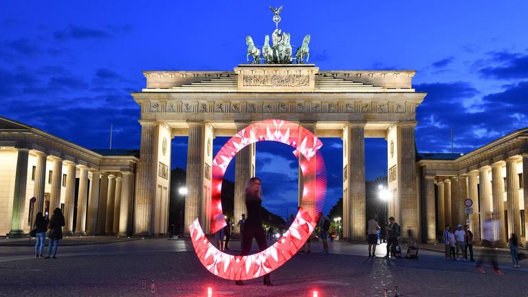 Eine Lichtkünstlerin zaubert mit roten Lichtern einen Leuchtkranz vor das Brandenburger Tor.