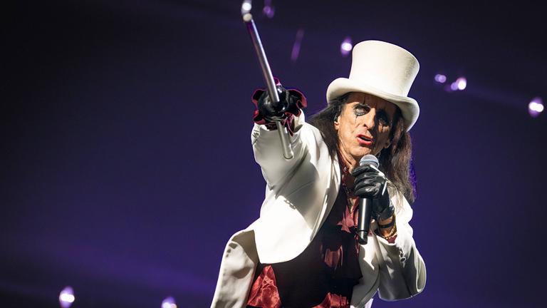 Alice Cooper in weißer Jacke und weißen Hut gekleidet mit Spazierstock in der Hand singt bei seinem Auftritt für "Die Night of the Proms" in der Festhalle Frankfurt