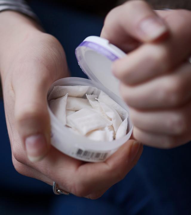 Eine Frau öffnet eine Dose mit tabakfreiem weißen Snus.