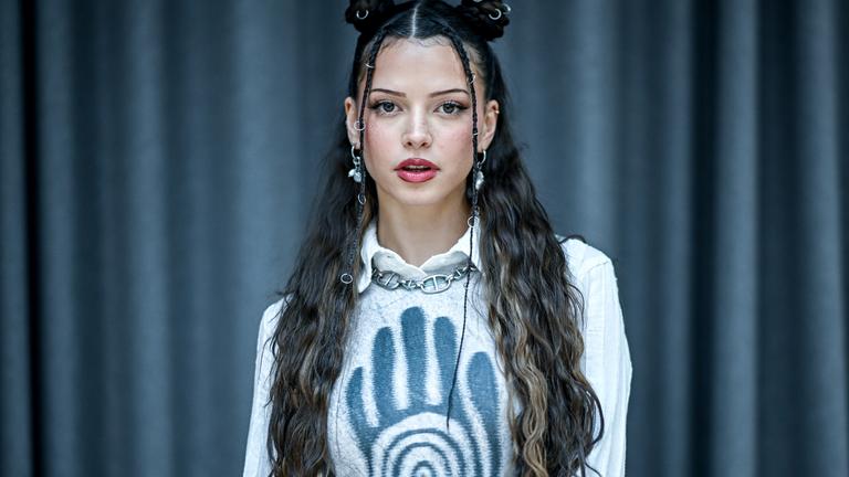 Nina Chuba steht vor einem schwarzen Vorhang. Das Bild ist im Porträtformat aufgenommen.