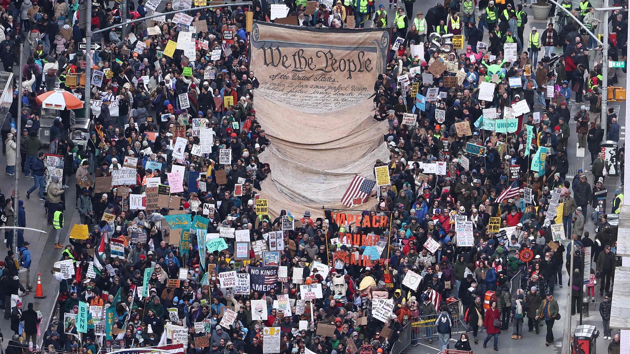 Demonstranten, die ein großes Schild mit der Abbildung der Unabhängigkeitserklärung halten, marschieren am 28. März 2026 während des nationalen Protesttages „No Kings“ in New York in der Nähe des Times Square.