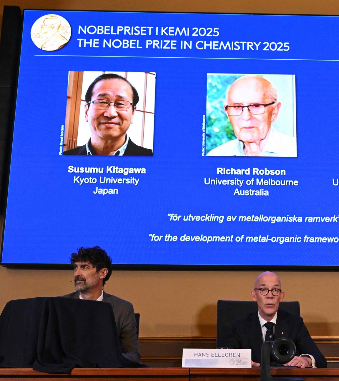 Die Bekanntgabe des Nobelpreises für Chemie 2025 - die drei Gewinner sind auf einer großen Leinwand zu sehen.