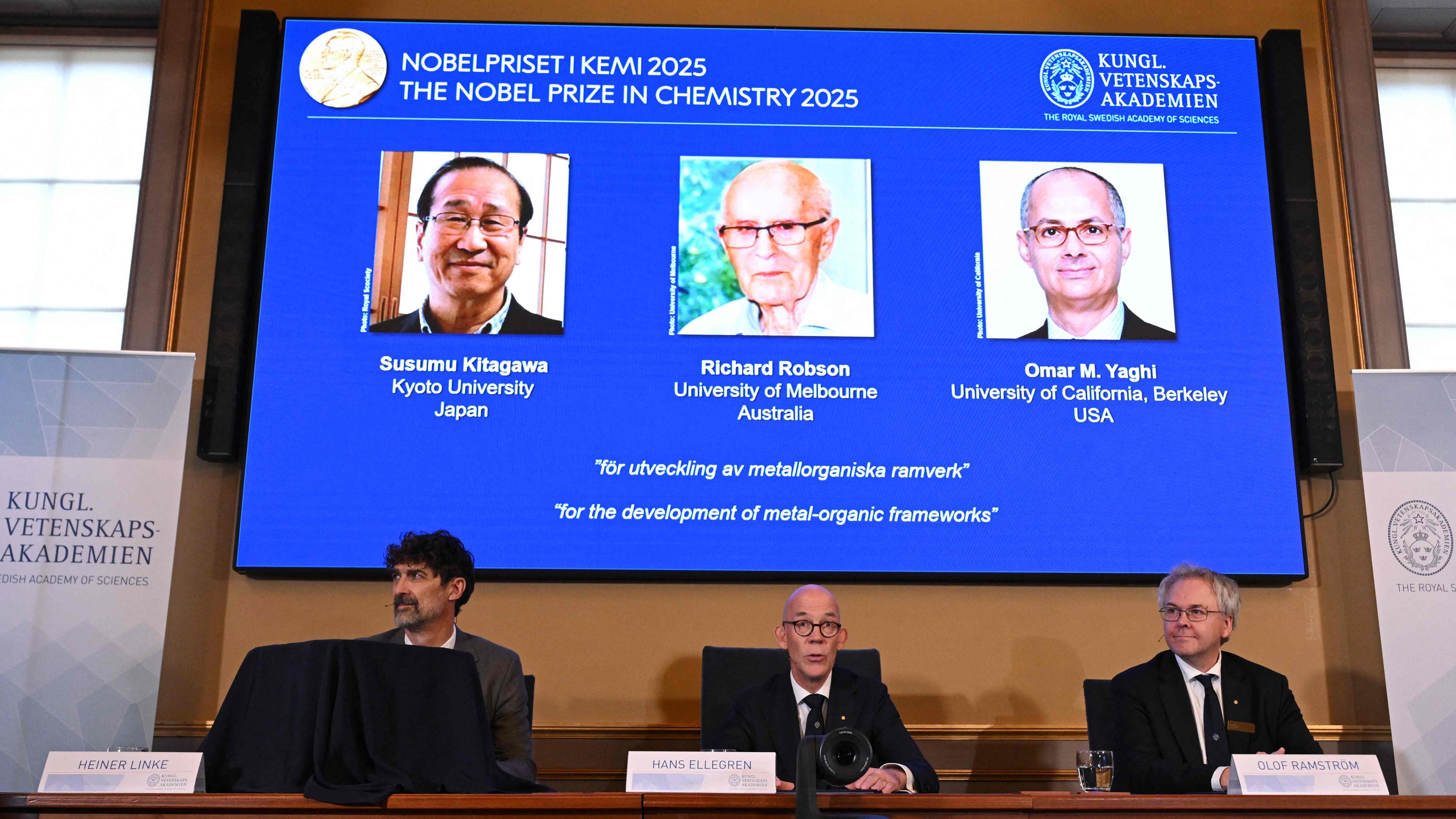 Die Bekanntgabe des Nobelpreises für Chemie 2025 - die drei Gewinner sind auf einer großen Leinwand zu sehen.