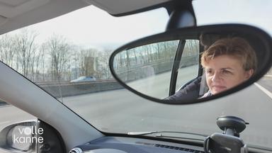 Frau fährt Auto, man sieht ihr Gesicht im Innenspiegel des Autos. 