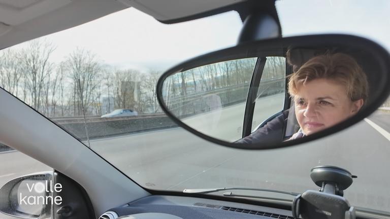 Frau fährt Auto, man sieht ihr Gesicht im Innenspiegel des Autos. 