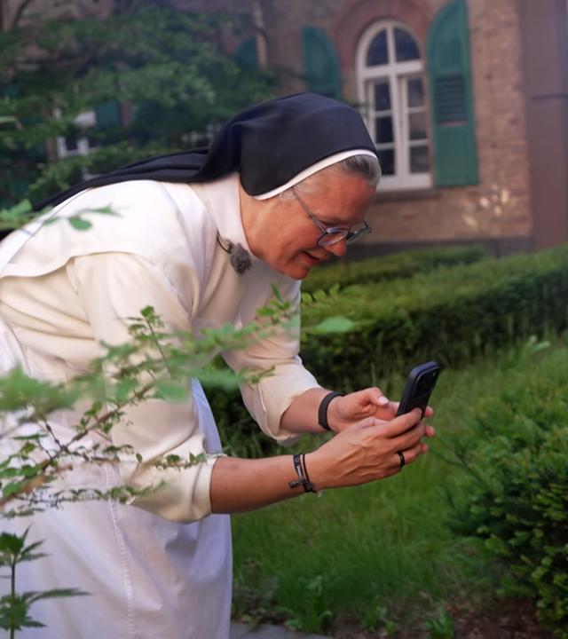 Eine Nonne filmt gerade mit ihrem Handy im Garten.