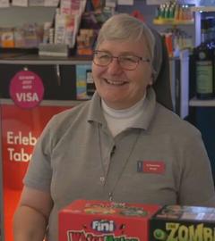 Birgit Baier im "Büdchen" in Gelsenkirchen. Im Innenraum reihen sich bunte Kühlschränke mit Bier und Softdrinks an Regale mit Zigaretten, Instant-Nudeln und Proteinriegeln. 