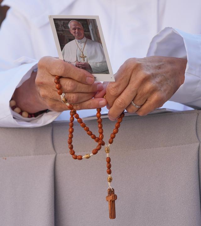 Eine Nonne hält ein Bild von Papst Leo XIV. und einen Rosenkranz.