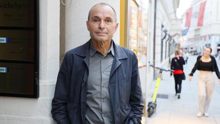 Ein älterer Mann imd unkelgrauen Anzug steht an einer Straßenecke.