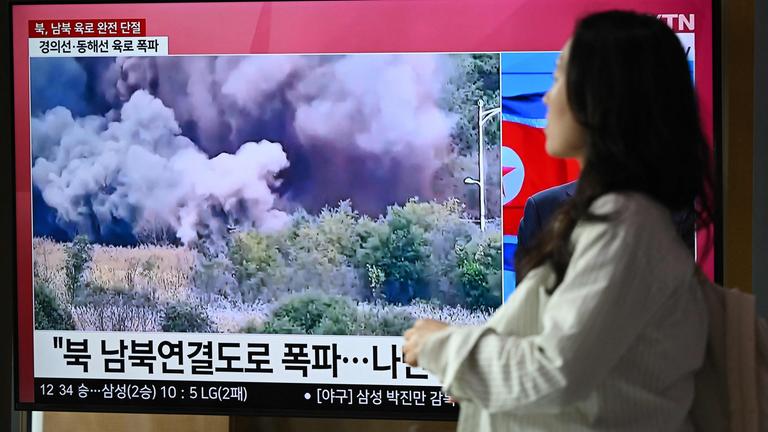 Eine Frau geht an einem Fernsehbildschirm vorbei, auf dem eine Nachrichtensendung mit Aufnahmen einer Explosion auf einer Straße zwischen Nord- und Südkorea am 15. Oktober 2024 an einem Bahnhof in Seoul am 16. Oktober 2024 gezeigt wird