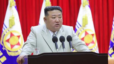 Kim Jong-un steht vor drei Mikrofonen im hellen Anzug.