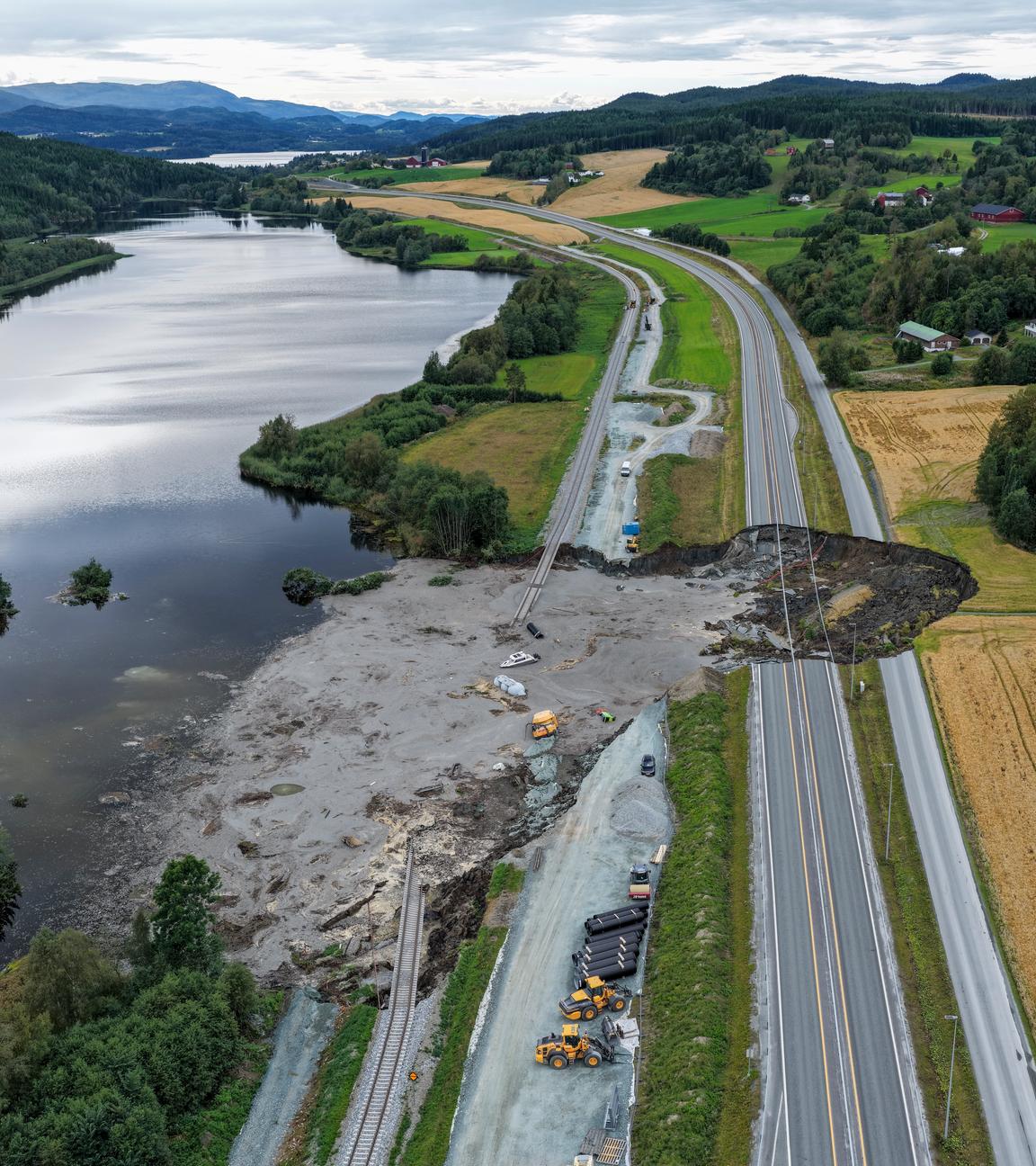 Von einem großen Loch in einer Landstraße aus fließt schlamm in einen anliegenden See.
