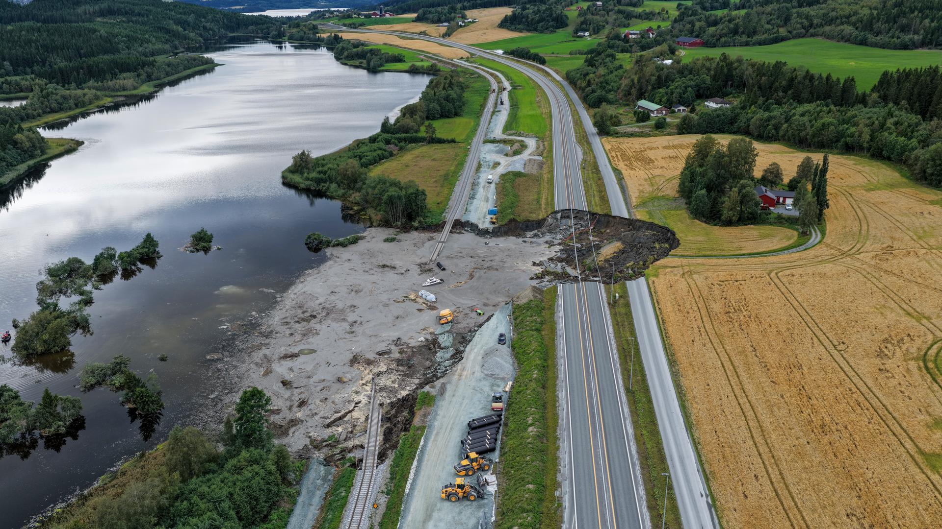 Von einem großen Loch in einer Landstraße aus fließt schlamm in einen anliegenden See.