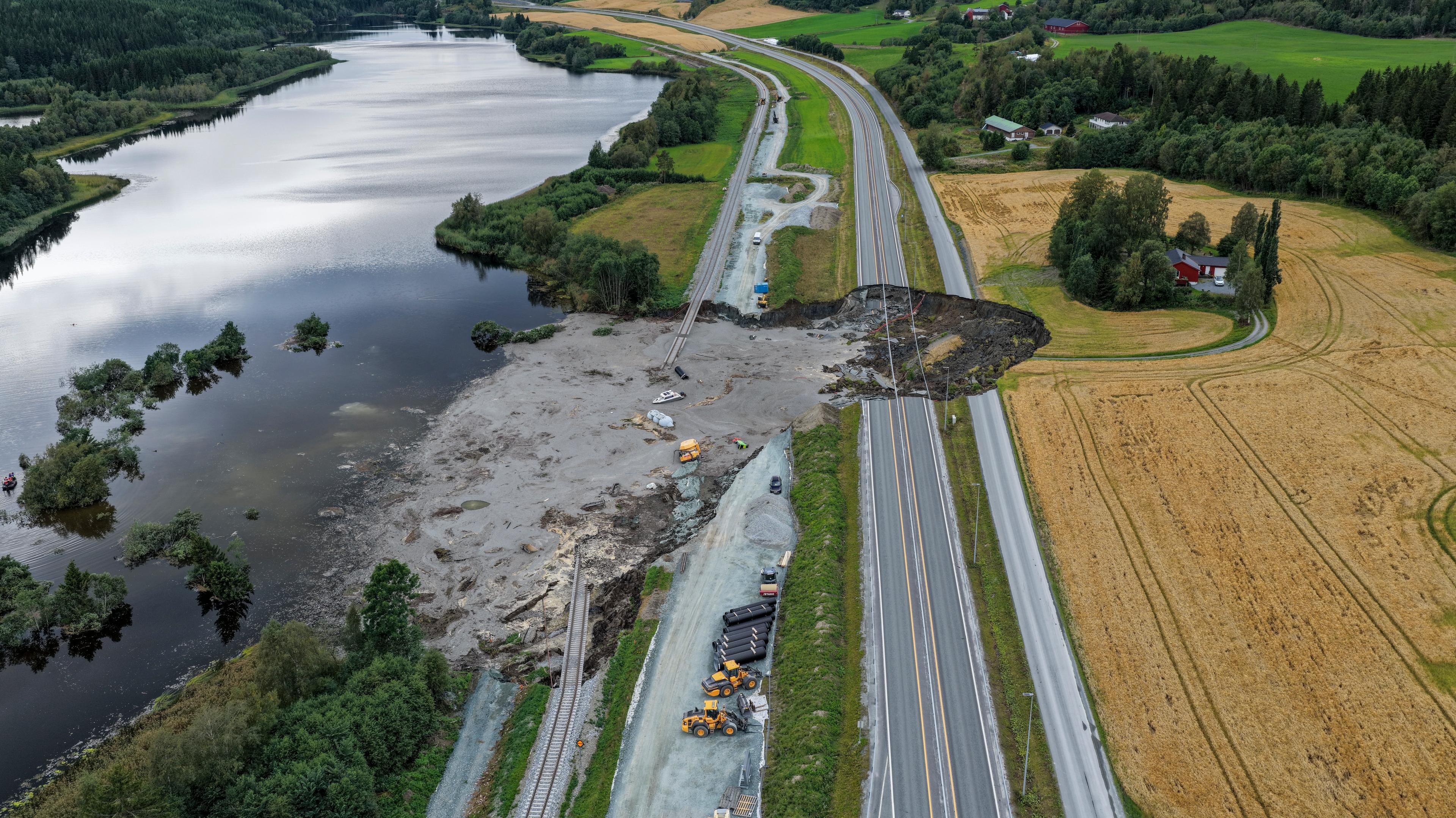 Von einem großen Loch in einer Landstraße aus fließt schlamm in einen anliegenden See.