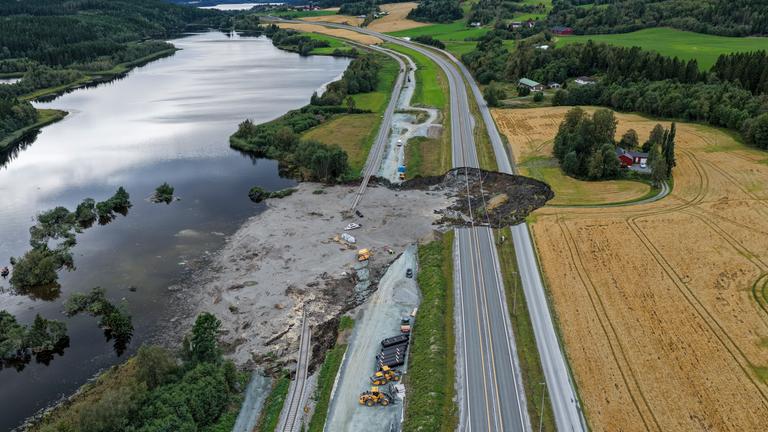 Von einem großen Loch in einer Landstraße aus fließt schlamm in einen anliegenden See.
