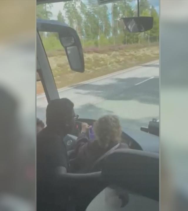 Zwei Passagiere sitzen am Lenkrad eines Busses und lenken diesen.