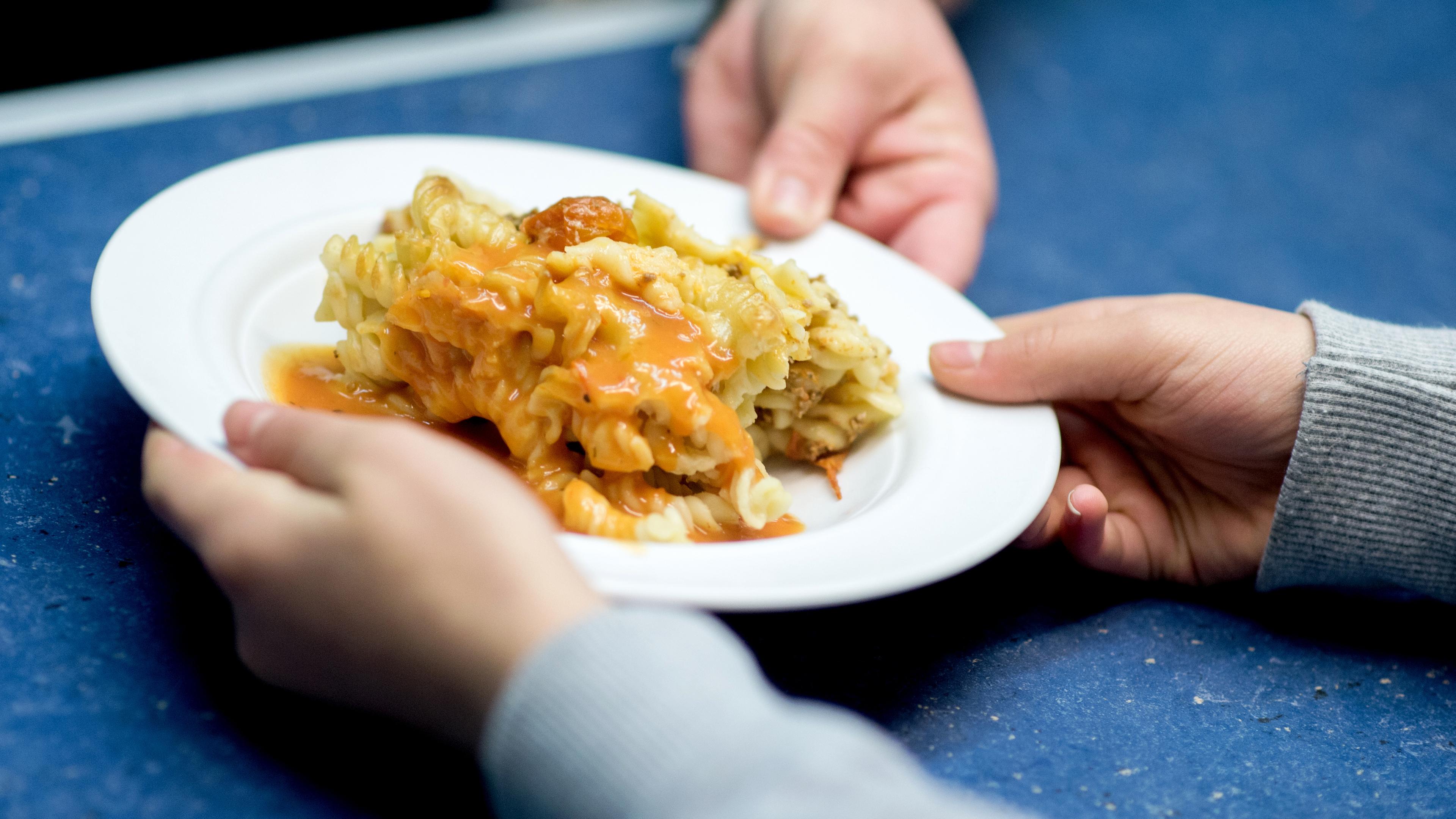 Nudelauflauf mit Soße, an ein Schulkind in der Mensa einer Grundschule.