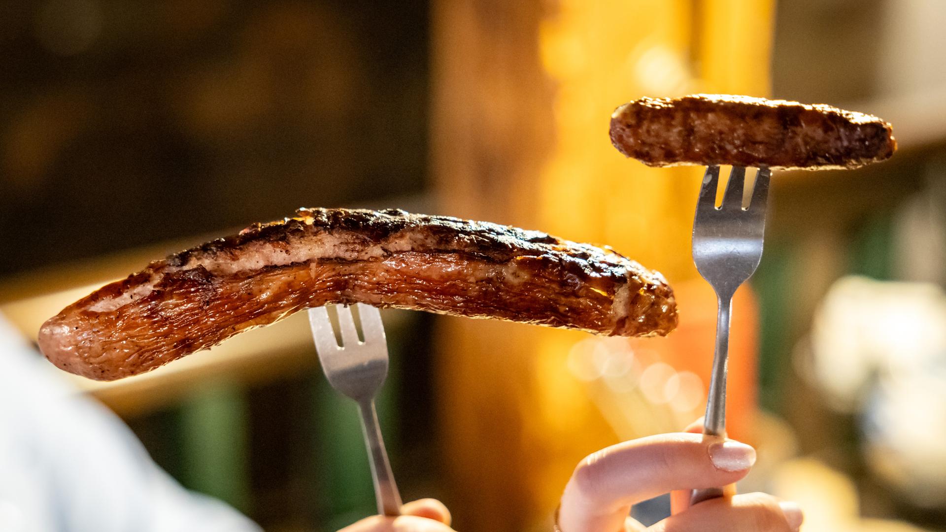 Bayern, Nürnberg: Eine Nürberger Bratwurst (r) und eine Thüringer Bratwurst, aufgespießt auf einer Gabel