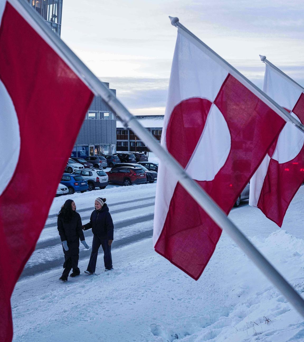 Frauen gehen am Mittwoch, dem 14. 1. 2026, in Nuuk, Grönland, vor Nationalflaggen auf einer Straße entlang. 