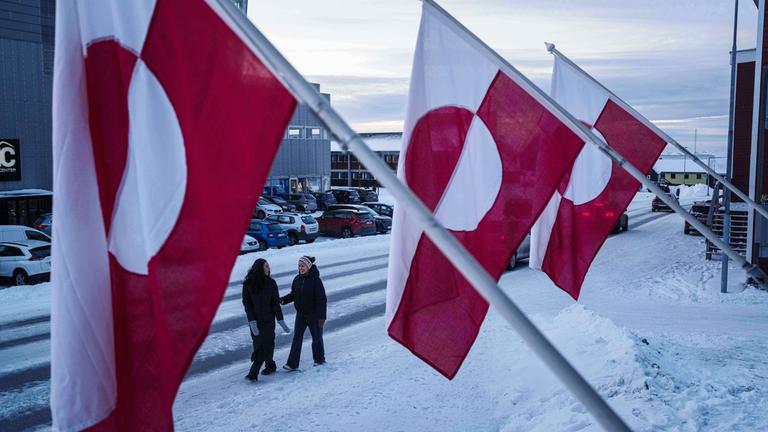 Frauen gehen am Mittwoch, dem 14. 1. 2026, in Nuuk, Grönland, vor Nationalflaggen auf einer Straße entlang. 