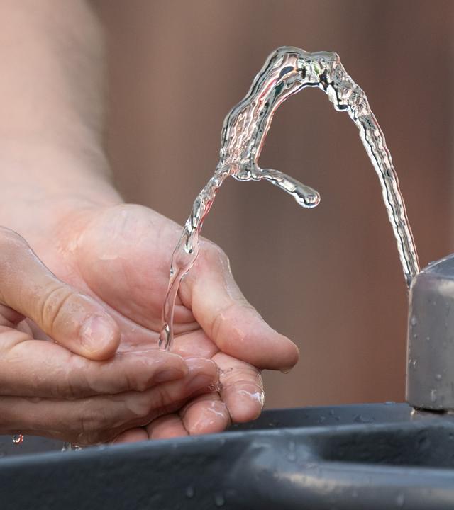 Ein Mann kühlt bei heißem Sommerwetter seine Hände an einem Trinkwasserbrunnen.