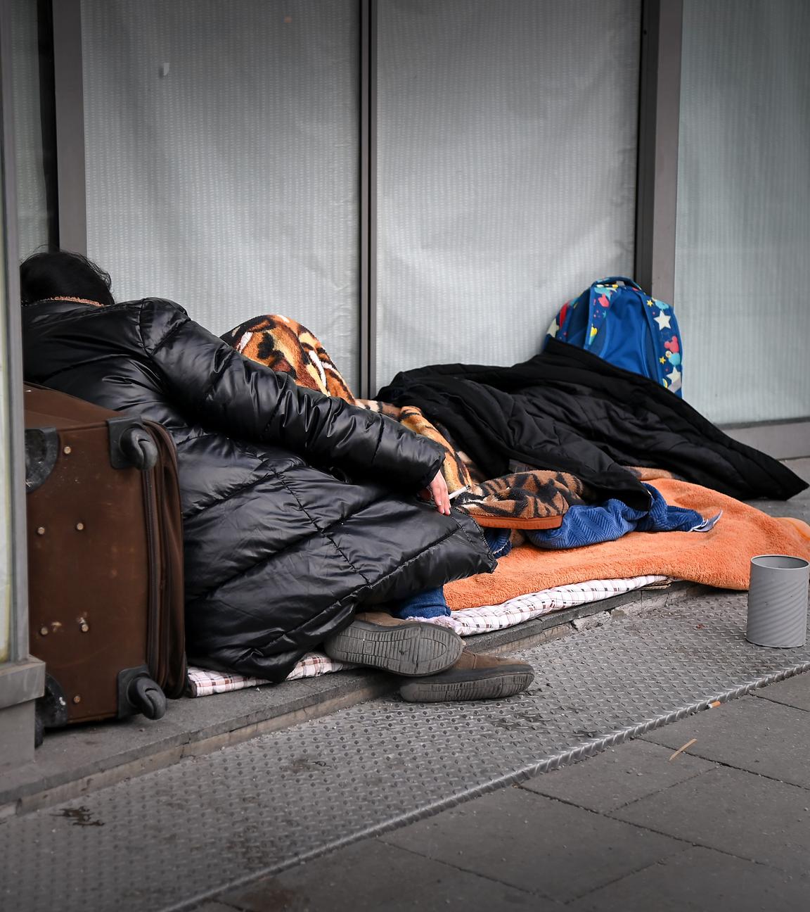 Obdachlose Person liegt eingewickelt in Decken.