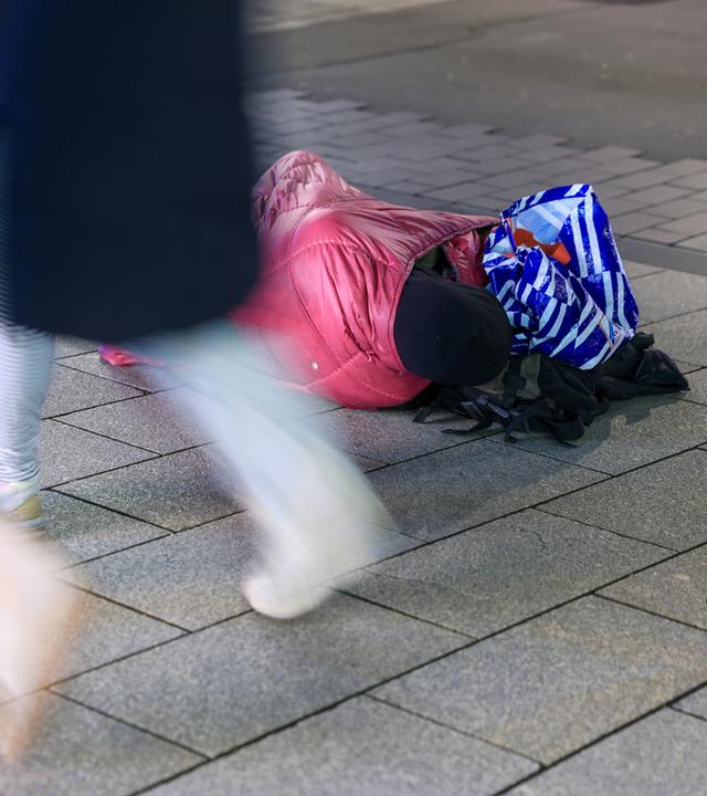 Ein Wohnungsloser liegt in eine Jacke gehüllt in einer Fußgängerzone während Passanten vorbeigehen am 27.10.2025 in Leipzig, Sachsen.